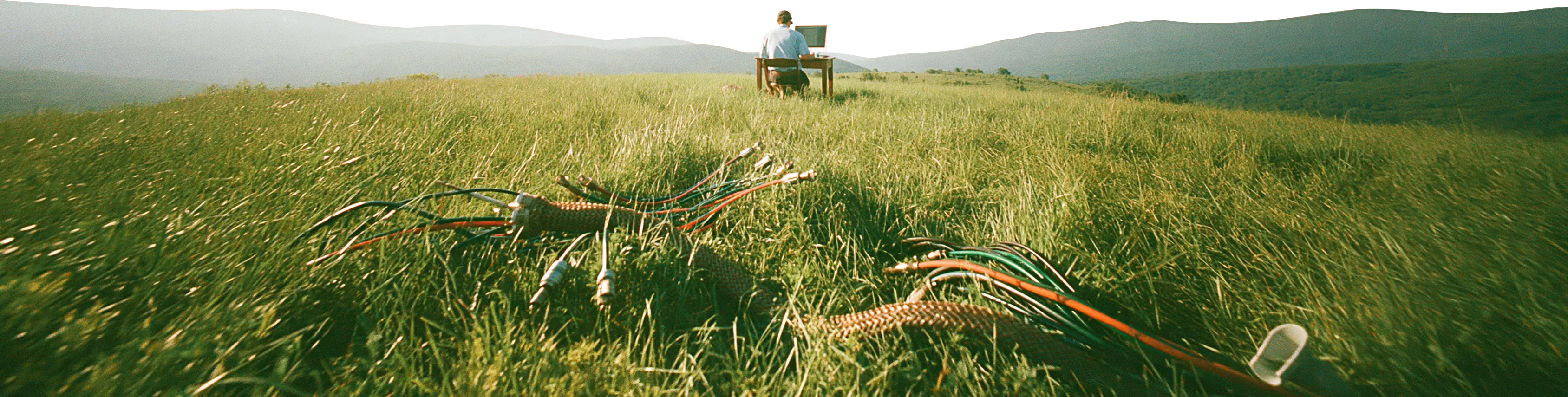 An engineer at a desk on a hilltop meadow, harnesses laid out in the grass